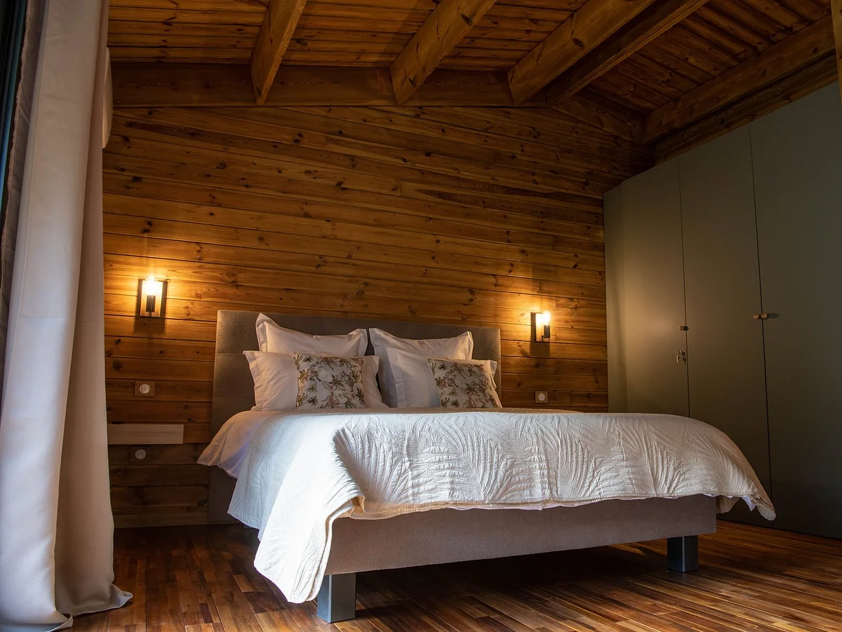 Un lodge, son grand lit et ses appliques allumées dans le bois