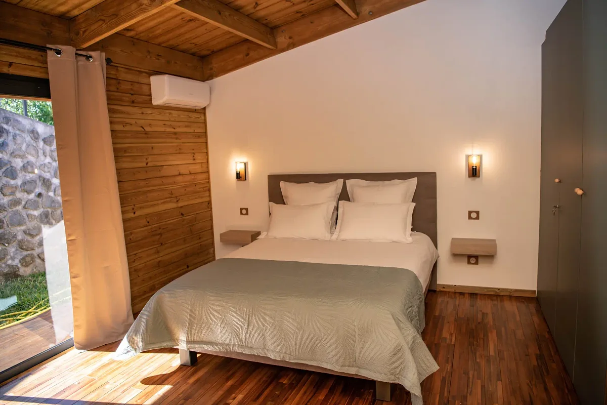 Le grand lit d'un lodge, ses coussins clairs et la lampe de chevet