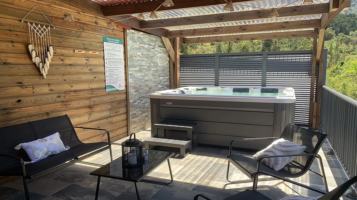 L'espace détente couvert, ses fauteuils et le jacuzzi derrière
